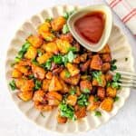 Overhead square shot of crispy air fryer diced potatoes garnished with herbs, plated with a small dish of ketchup and a fork resting on the side.