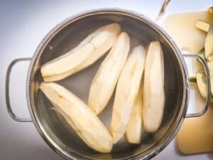 Peeled green bananas placed in a pot of cold water ready for cutting.