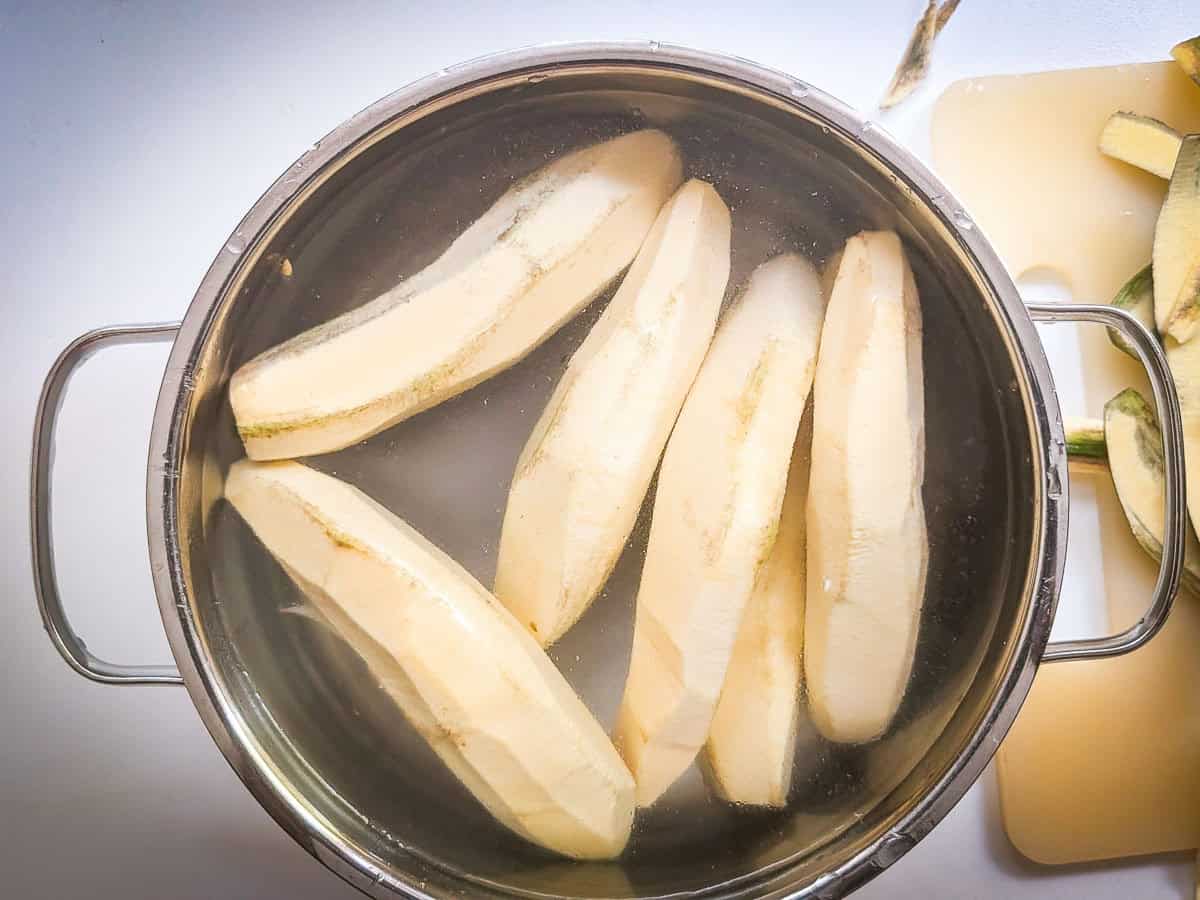 Peeled green bananas placed in a pot of cold water ready for cutting.