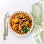 Matoke and beef stew served on a plate, garnished with some coriander leaves.