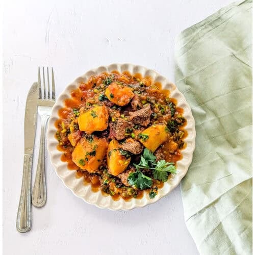 Matoke and beef stew served on a plate, garnished with some coriander leaves.