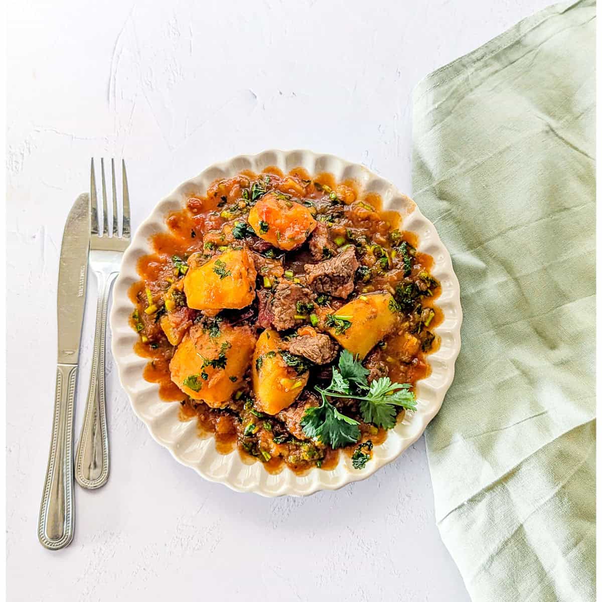 Matoke and beef stew served on a plate, garnished with some coriander leaves.