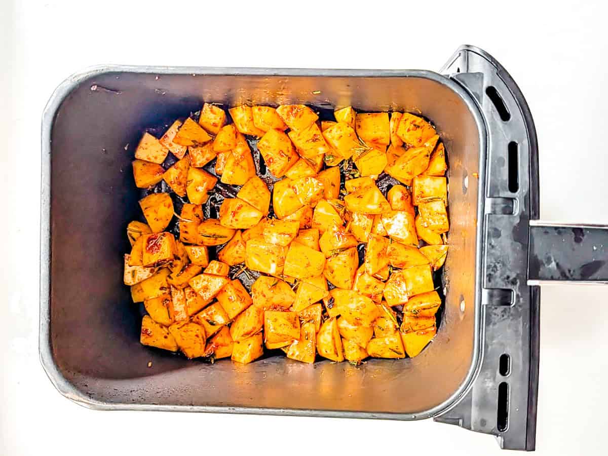Uncooked diced potatoes inside an air fryer basket.