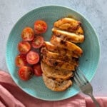 A close-up image of sliced chicken breast on a plate, with a fork resting on the plate.