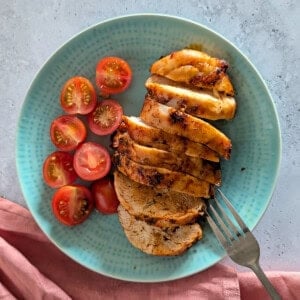 A close-up image of sliced chicken breast on a plate, with a fork resting on the plate.
