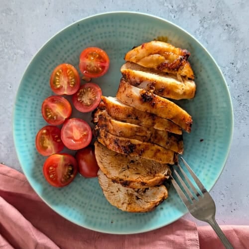 A close-up image of sliced chicken breast on a plate, with a fork resting on the plate.
