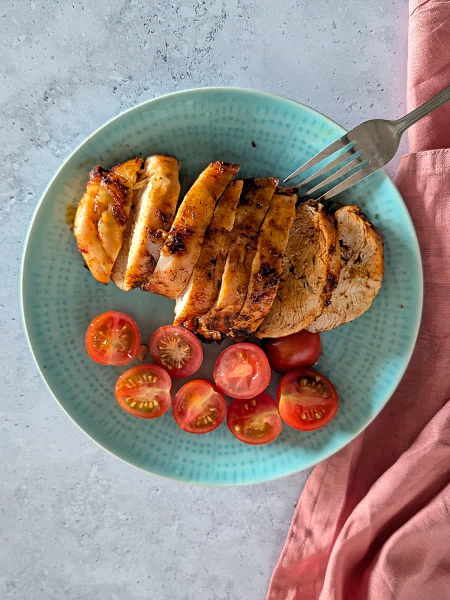 A top-down image of sliced golden-brown chicken breast served on a plate with halved cherry tomatoes.