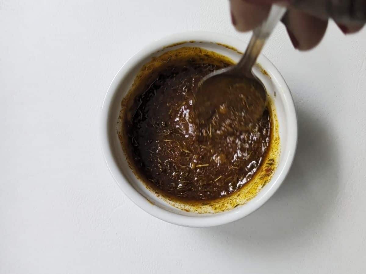 A top-down image of a bowl filled with a dark, seasoned marinade being stirred with a spoon.