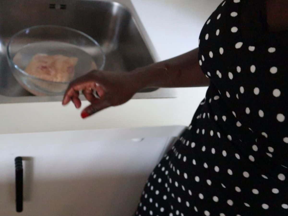 Preparing frozen chicken breast placed in a glass bowl near the sink.