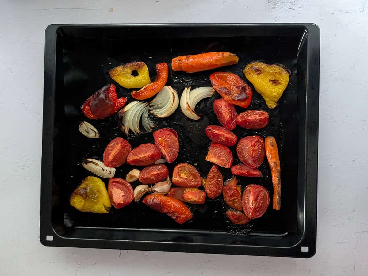 An overhead image of roasted tomatoes, bell peppers, carrots, onion, and garlic on a baking tray.