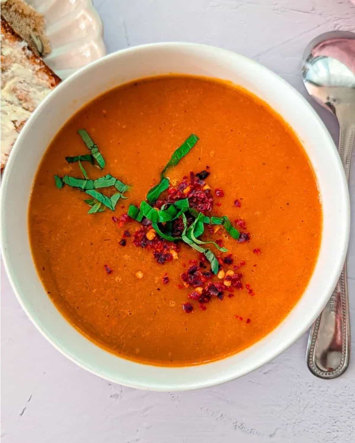 Soup maker roasted tomato soup served in a bowl, garnished with fresh basil and chili flakes.